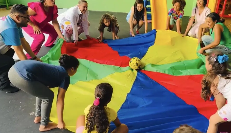 Crianças e terapeutas em atividade em grupo com paraquedas colorido na Clinfono